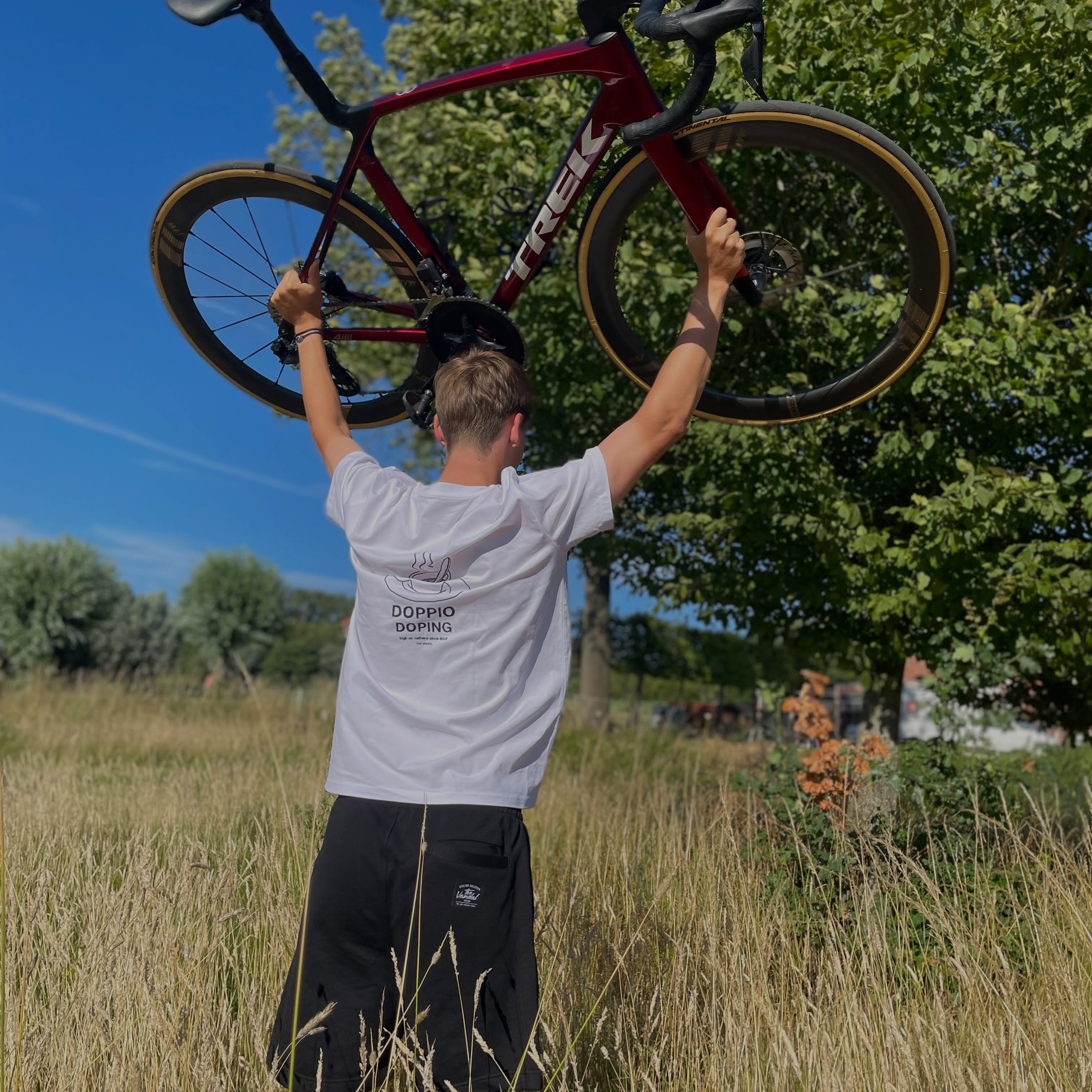 Wielrenner tilt zijn racefiets boven het hoofd in een veld, in The Vandal-tee